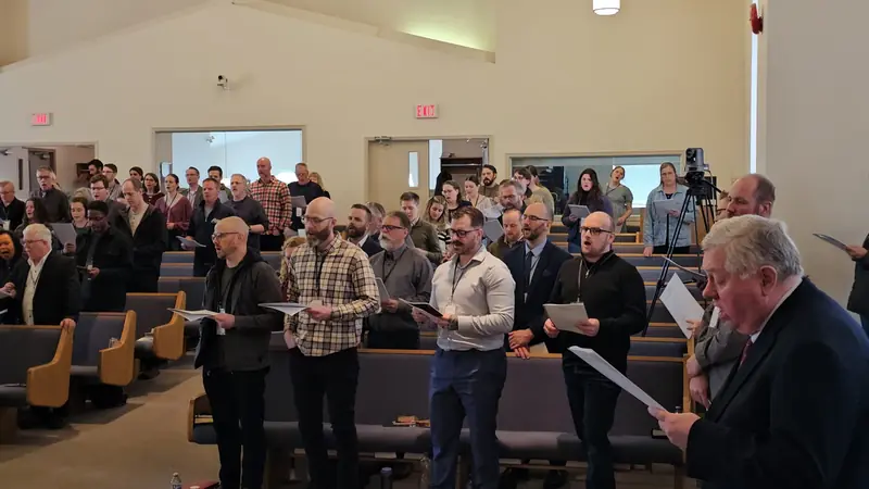 Pastors and church members standing together with service sheets during a conference session