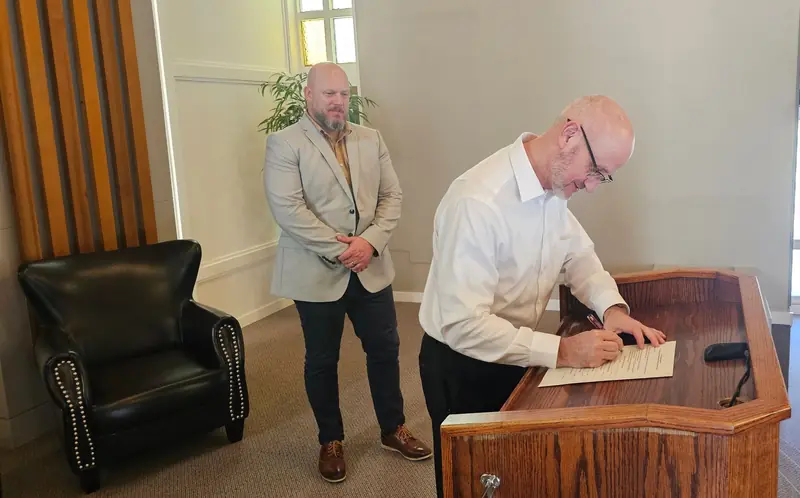 A pastor signing the ARBCWC founding agreement at the podium while another looks on